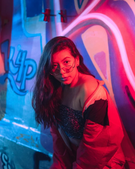 a woman leaning against a graffiti wall with purple light shining on her