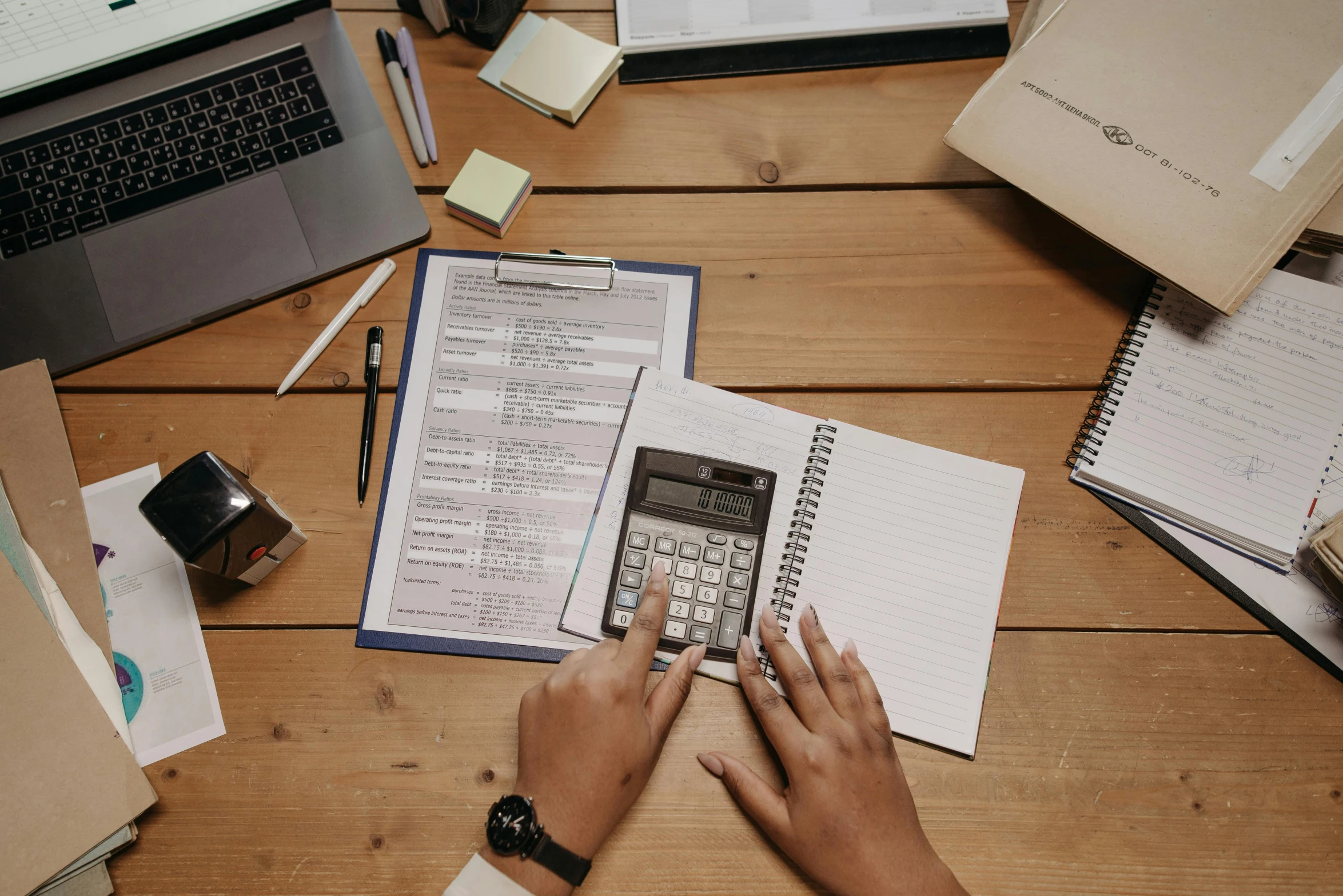 a person sitting at a table with a notebook, phone, and several open documents