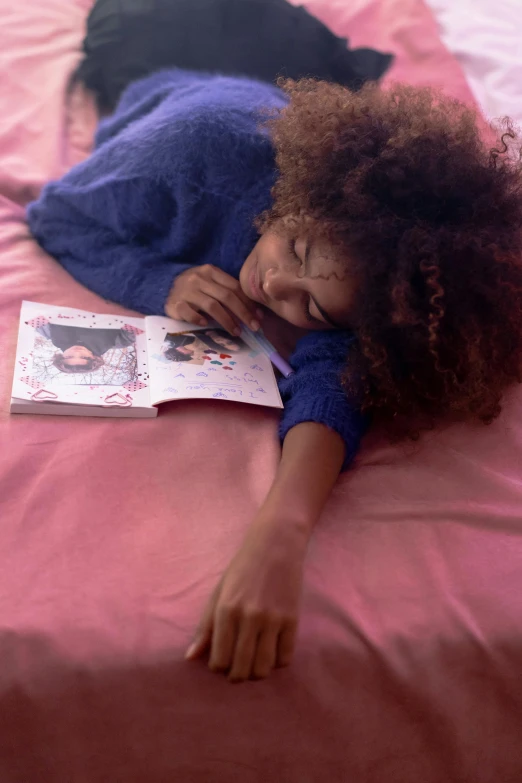a little girl laying on a bed next to a book