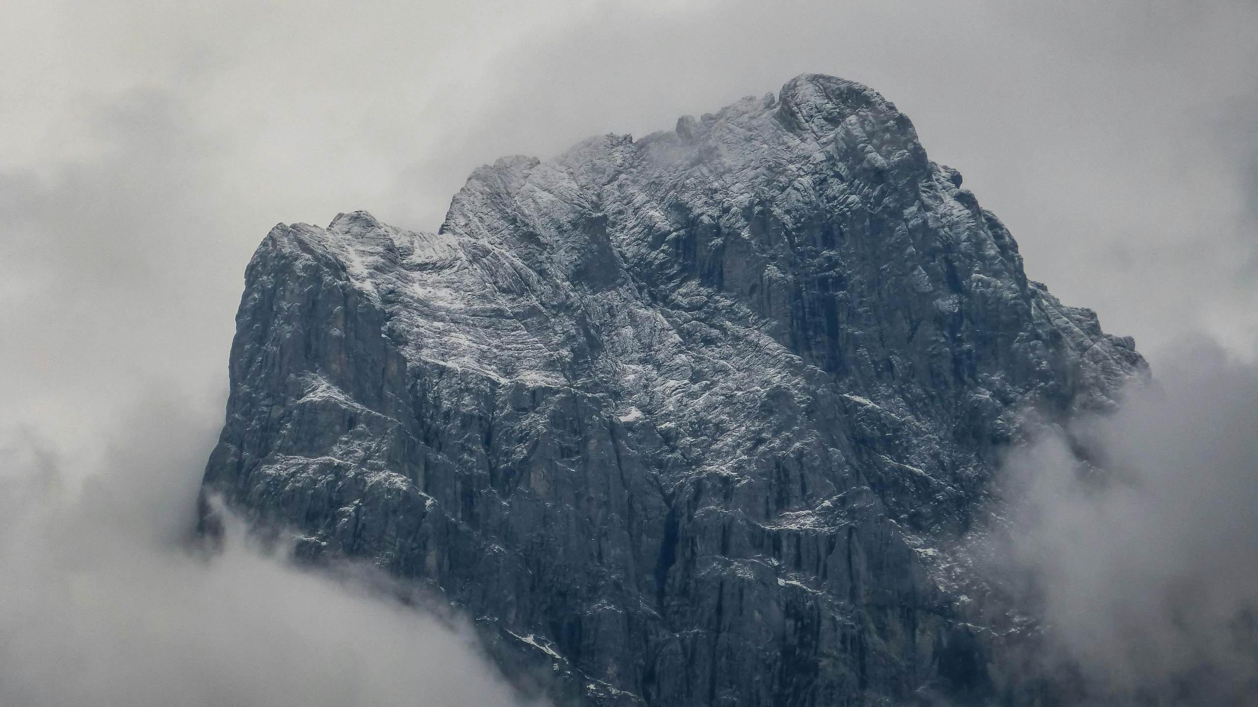 a mountain covered in snow and fog on a cloudy day