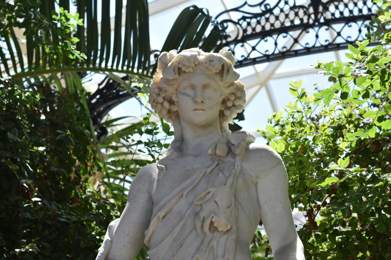 a statue surrounded by bushes and flowers under a sky tunnel