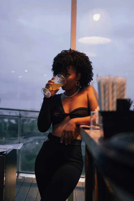 woman in black dress drinking at table next to window