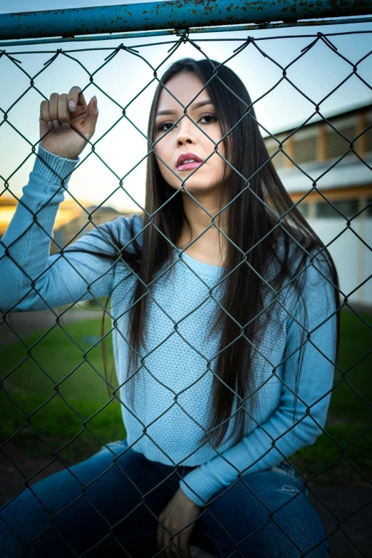 a young woman poses against a chain link fence