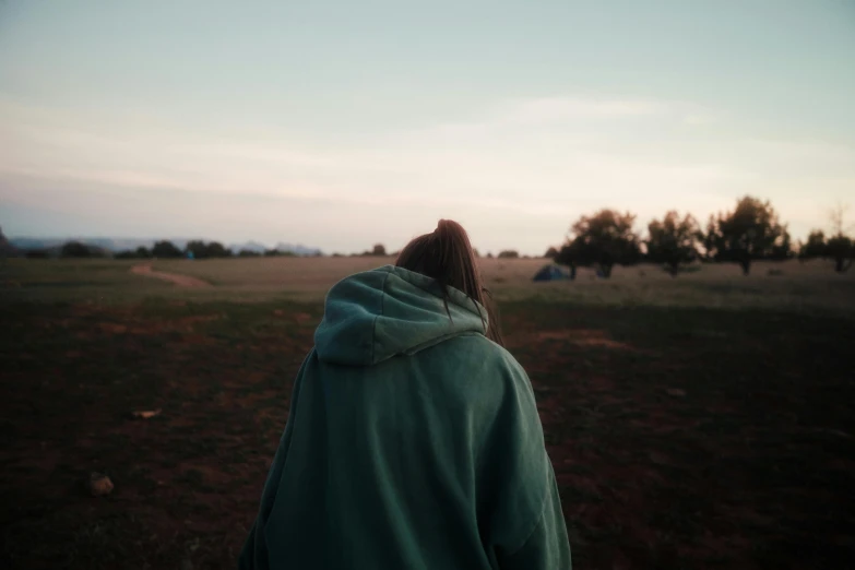 the back of a person wearing a hooded jacket in the middle of a field