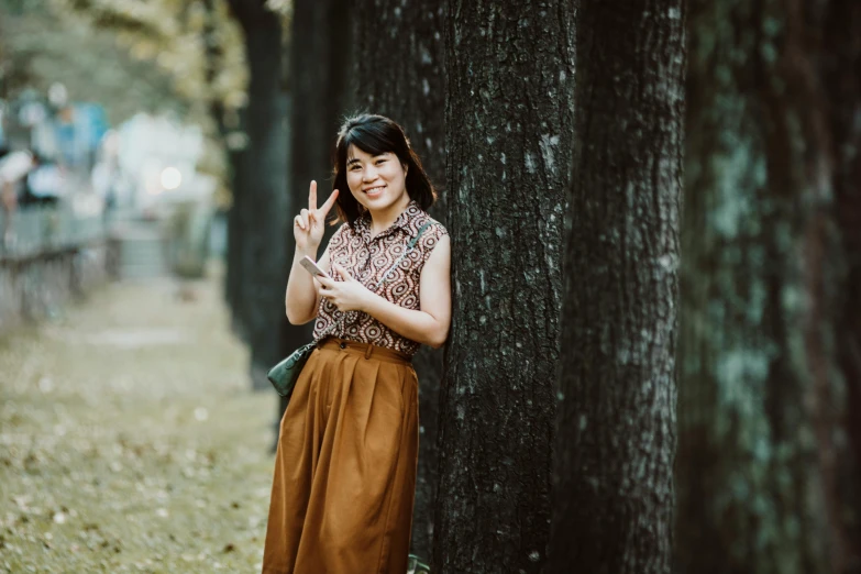 a young woman leaning against a tree gives the vulcan sign