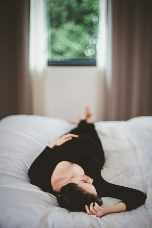 a woman laying on a bed in front of a window