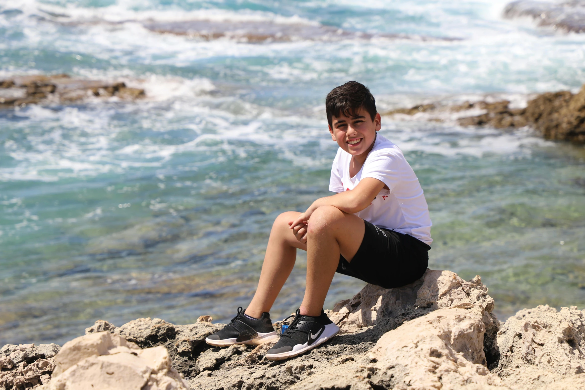 a young man sits on the rocks of a cliff by the ocean