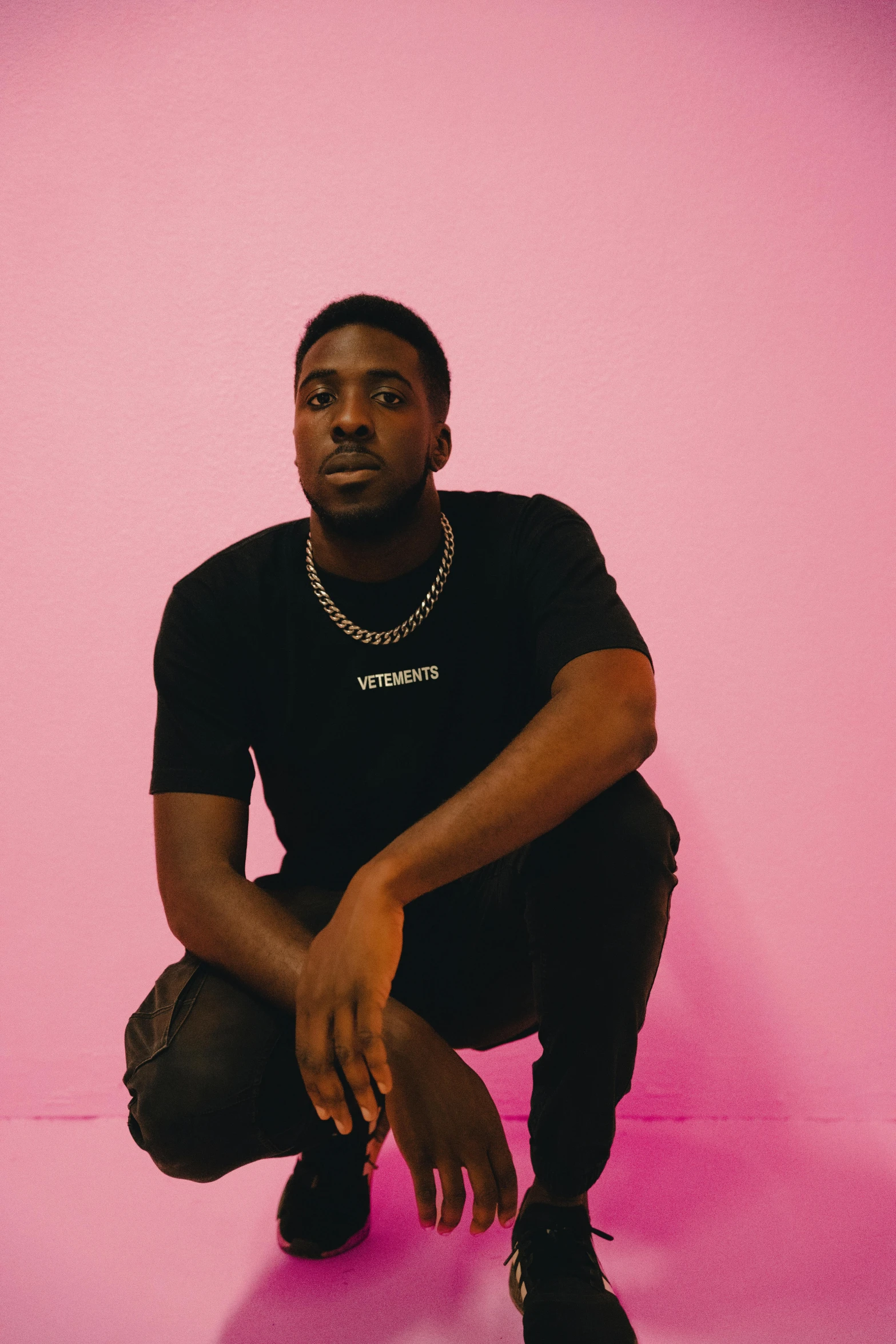 man in black shirt and pants sitting on pink background