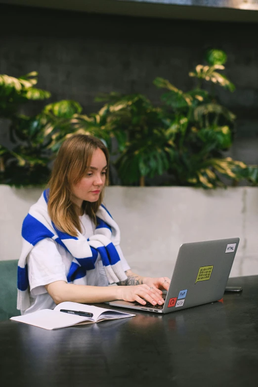 a woman is on a laptop in front of a green plant