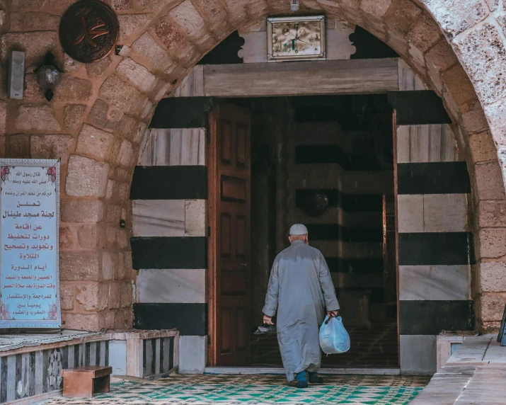 man wearing gray clothes standing in front of stone archway