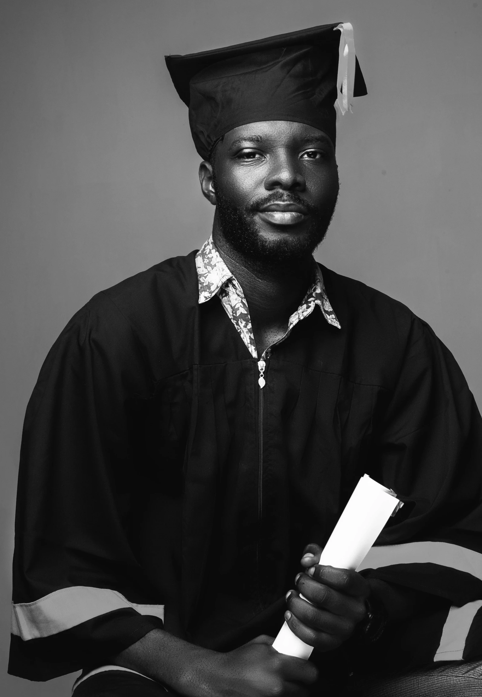 a man wearing a cap and gown holding a diploma