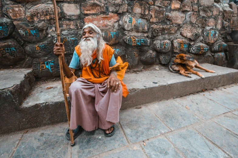 man with a white beard and beard sitting on a rock wall next to his dog