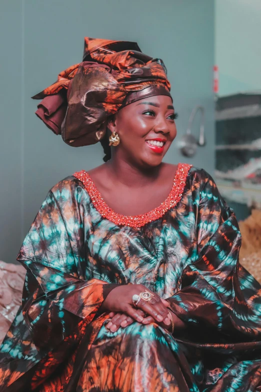 a smiling woman sitting in a bedroom with her head scarf on