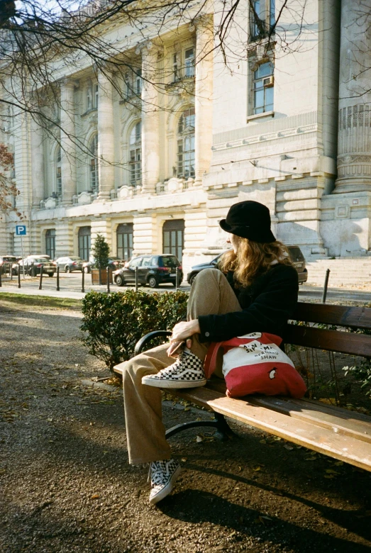 woman sitting on wooden park bench in front of large building