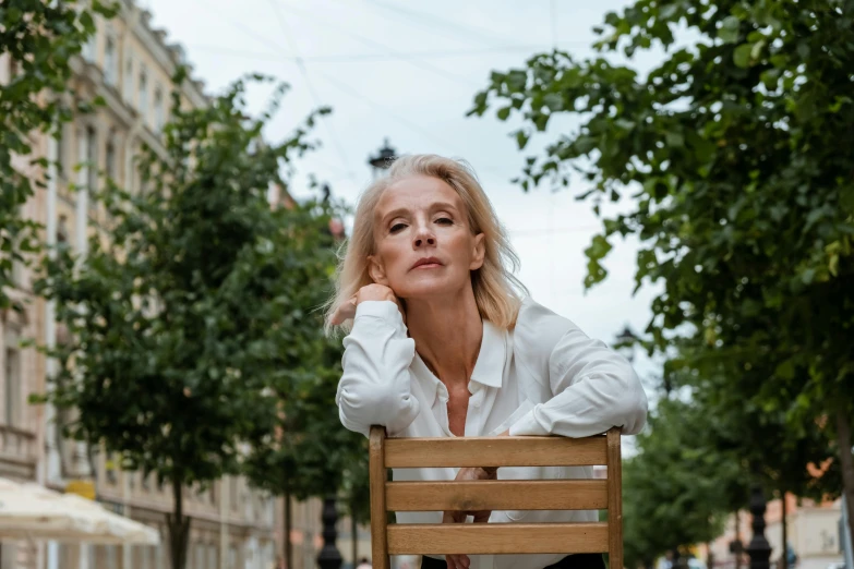 a blonde woman sitting in a wooden chair next to some trees