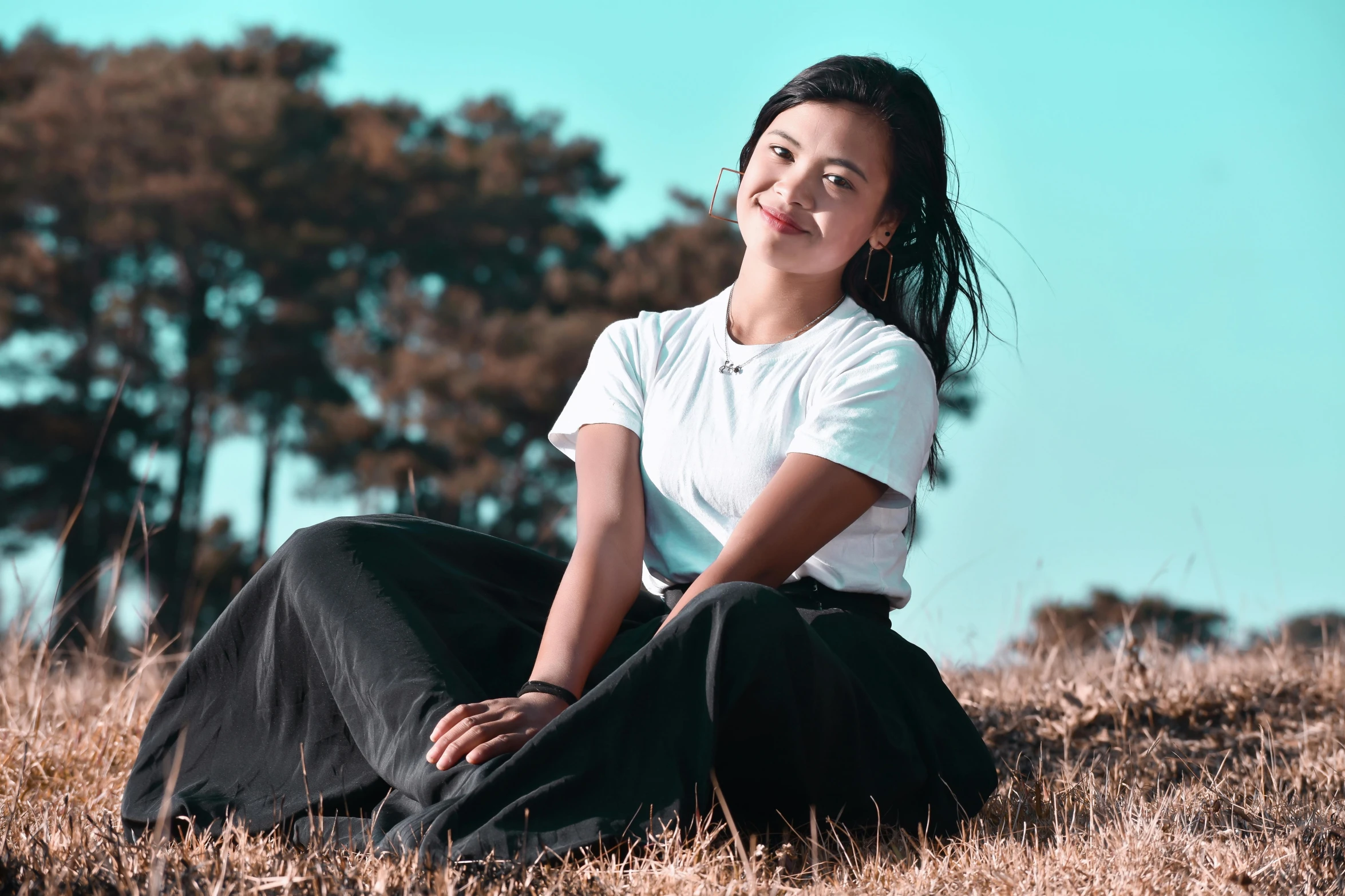 a beautiful young woman sitting on a grass covered field