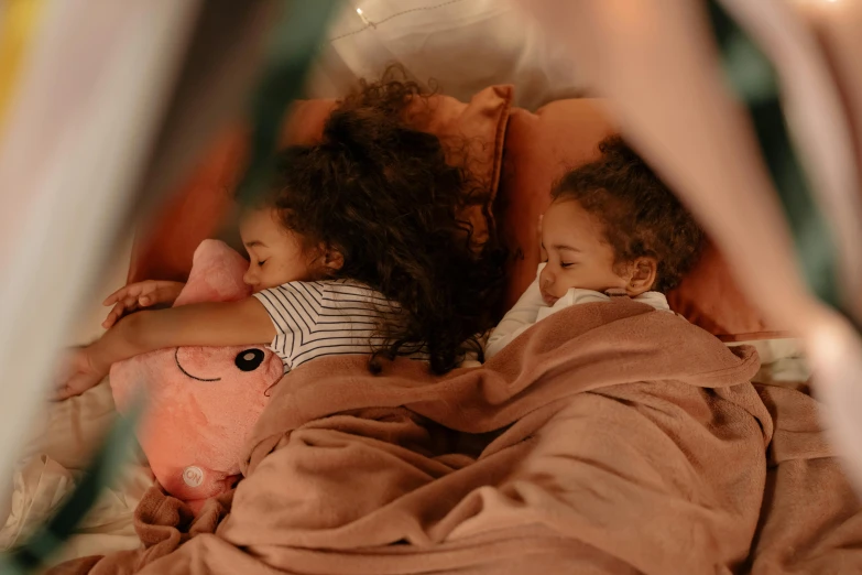 two children lying in a bed, one with a stuffed animal