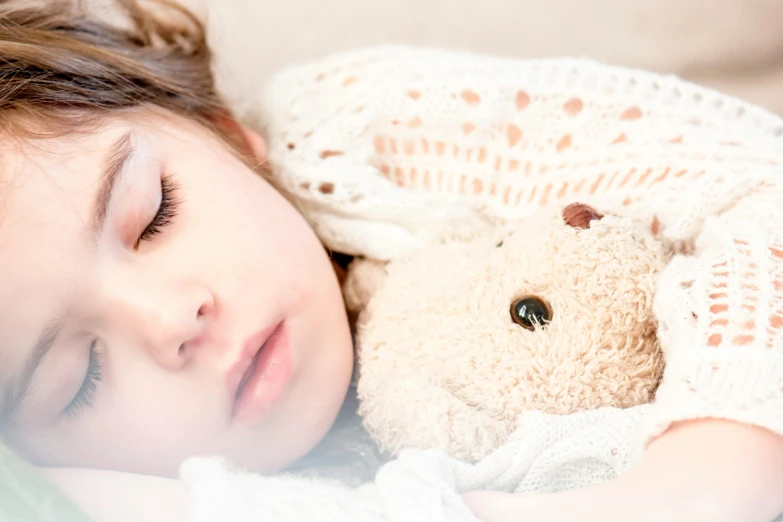 a child laying in bed next to a teddy bear