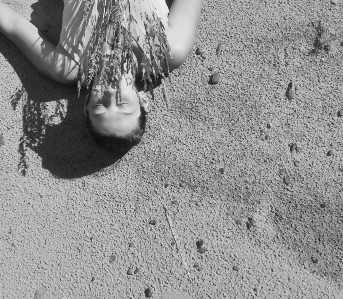 a girl laying on the sand with some grass