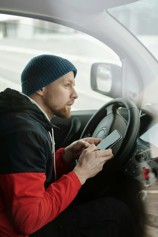 a man in a blue beanie is sitting inside of a car holding a cell phone