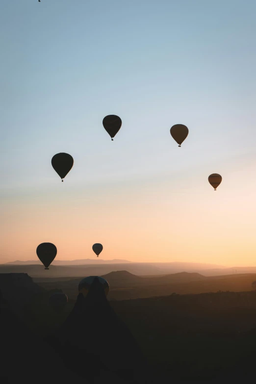 the silhouette of a person standing under several  air balloons