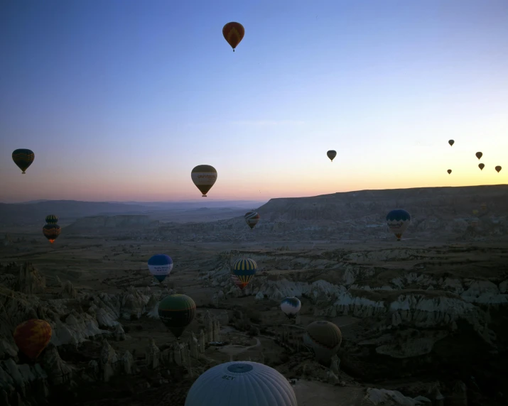 balloons fly over the rocky landscape at dusk