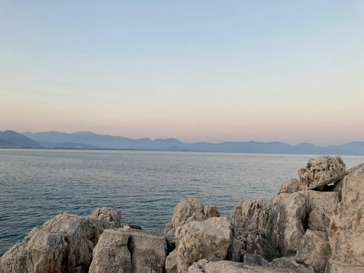 a rocky shoreline with blue water and a mountain in the background