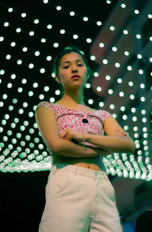 young woman standing with arms crossed near a light decoration