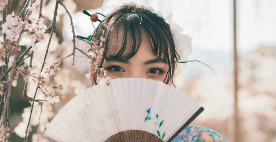 a woman holding a white fan under her face