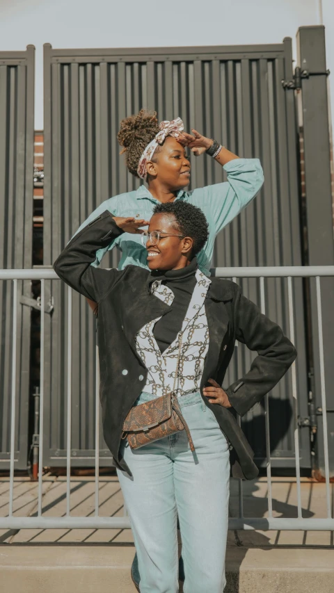 two women standing next to each other by a fence