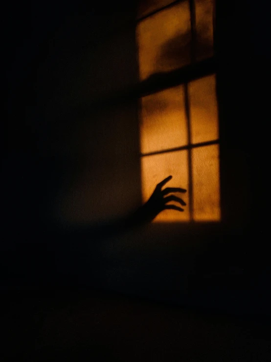 silhouette of person reaching toward open window at night