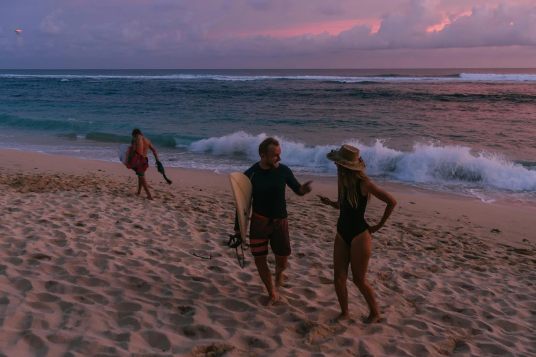 people standing on the beach at sunset, holding surfboards