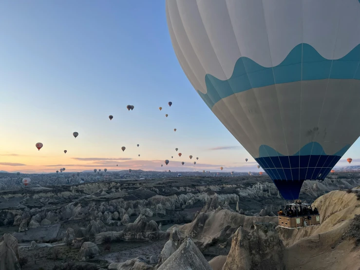 the sky has many balloons in it and they are flying above a rocky terrain