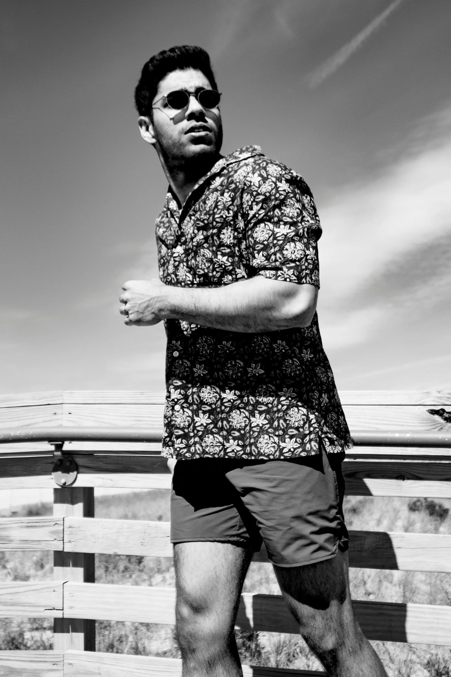 man in floral shirt posing by wooden bench at ocean