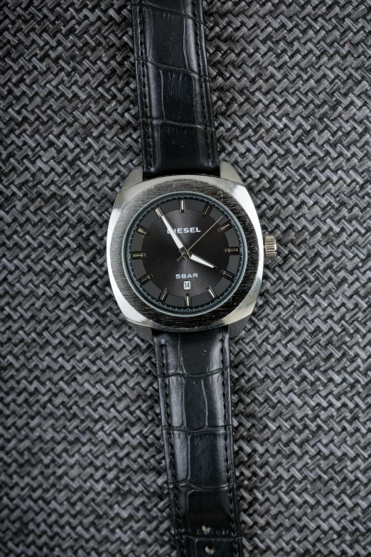 an analog black watch on grey fabric