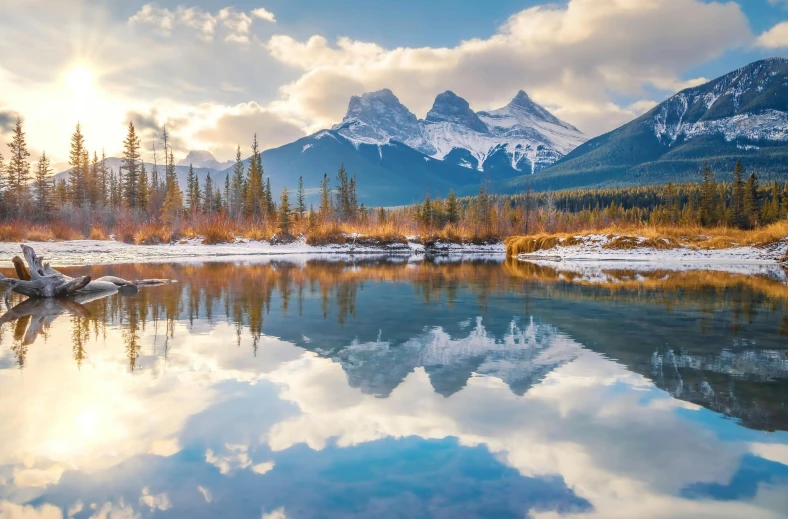 the sun shining over mountains and trees in the water