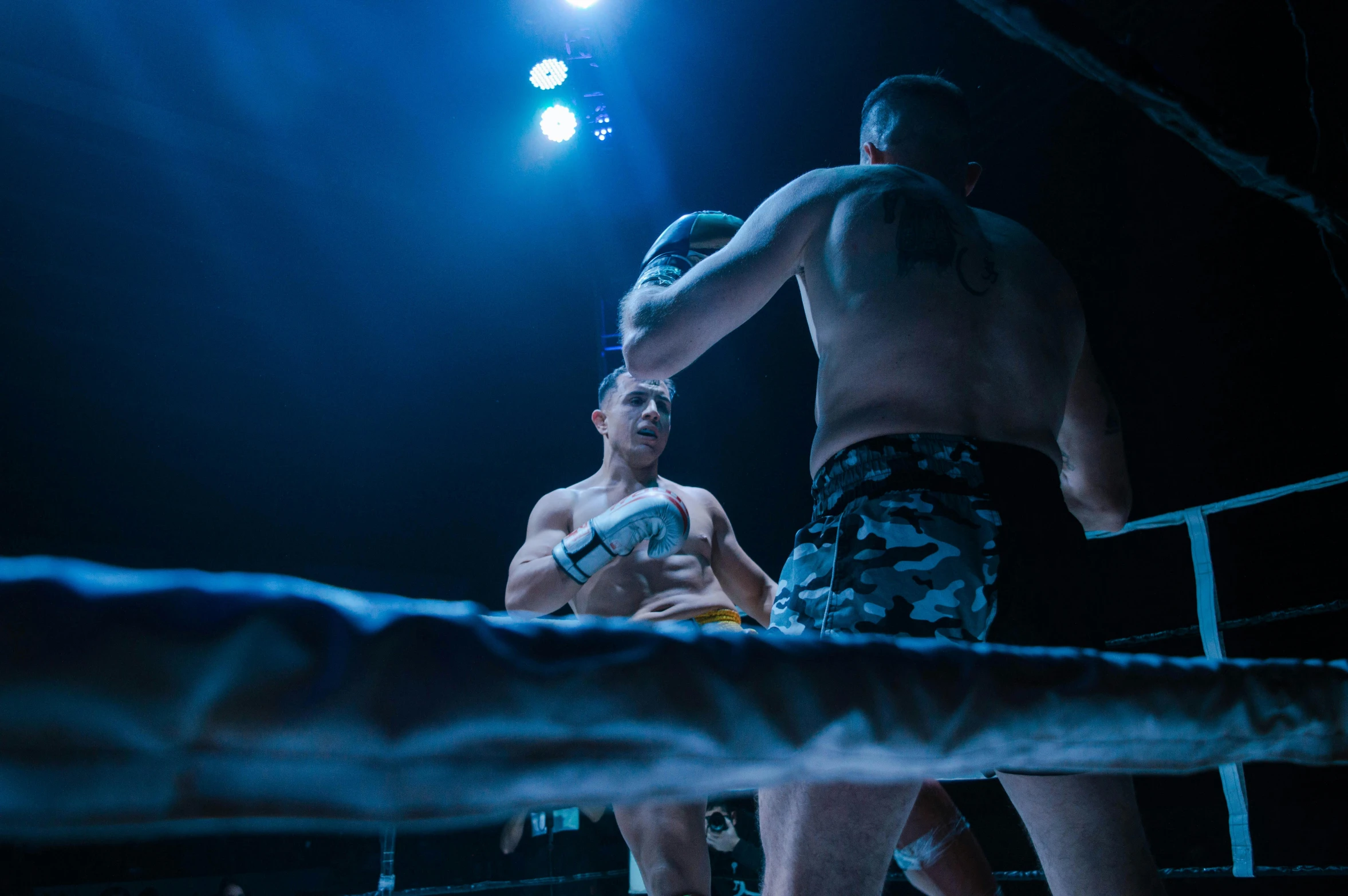 the men are wrestling in a dark boxing ring