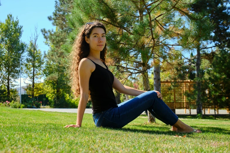 woman sitting on the ground in a park with her hands up to her chest