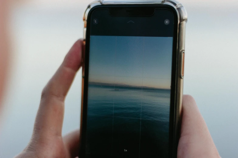 a person holding a cell phone over the top of a body of water