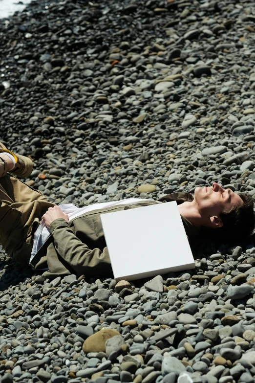 man laying on rocky beach next to laptop computer