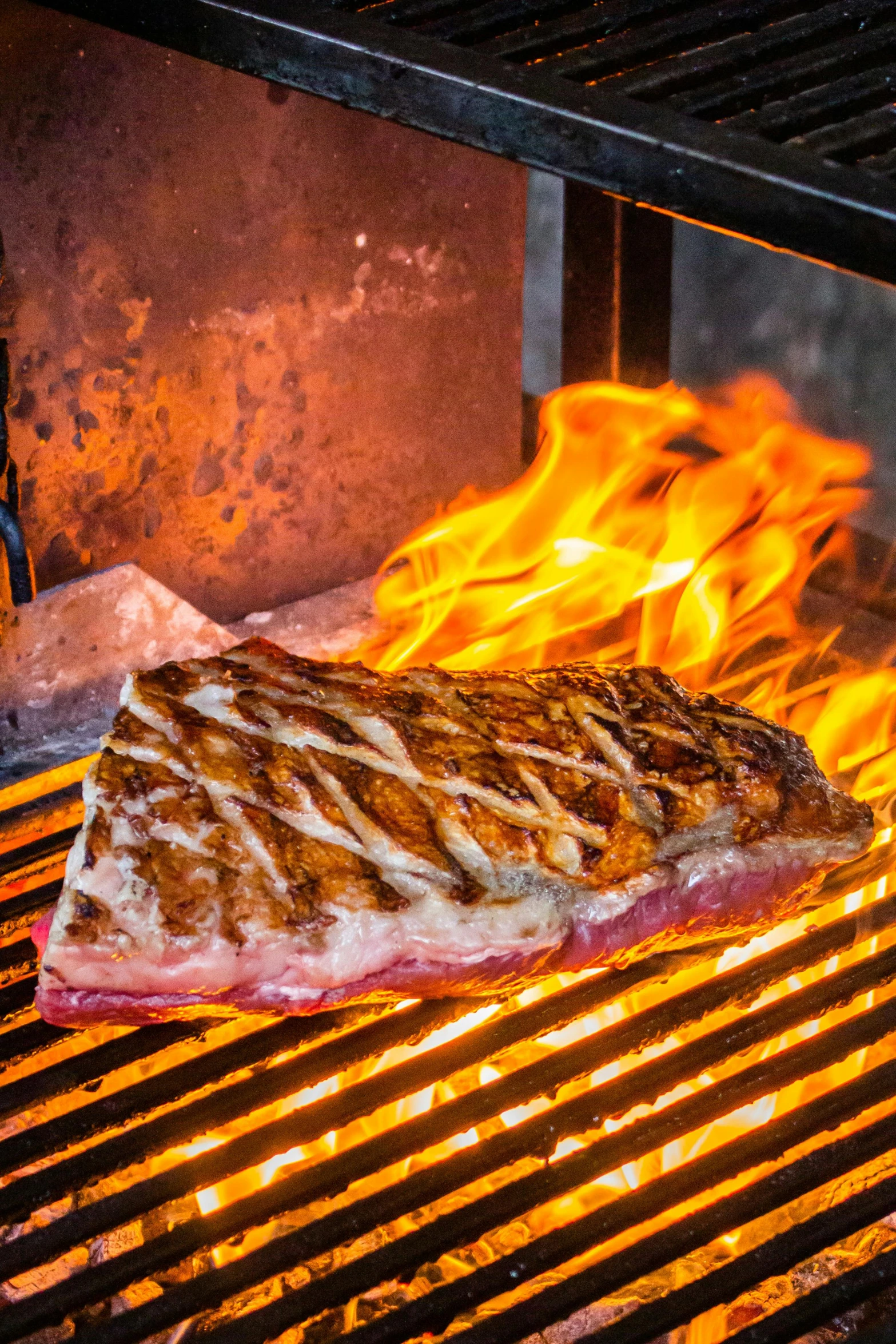 a steak cooking on the grill in front of flames