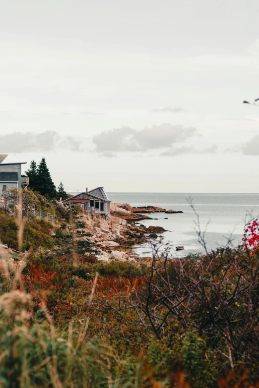 a house sits atop the edge of a grassy hill overlooking the ocean