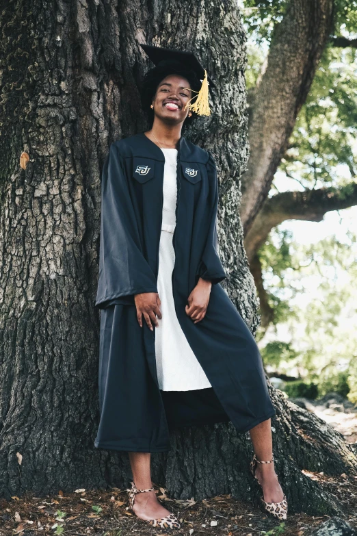 a man wearing a long jacket standing by a tree