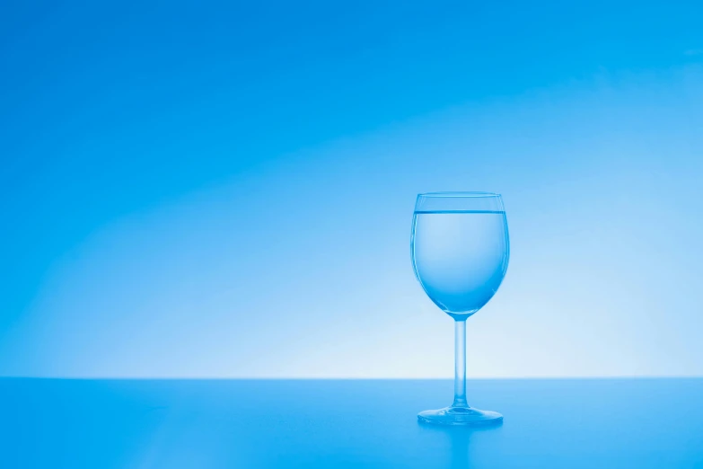 a glass on a table, the glass has a small amount of blue water inside of it