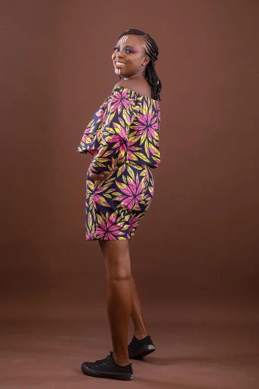 a woman standing in front of a brown background wearing a black dress with a pink flower print