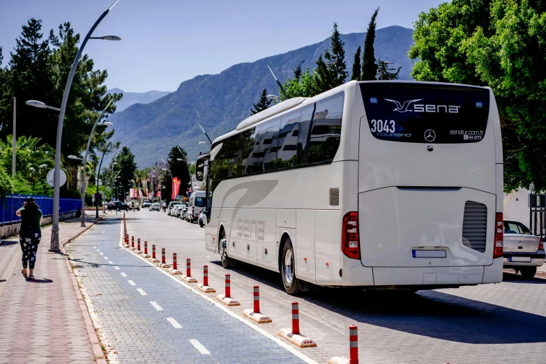 a large white bus traveling down a street next to tall mountains