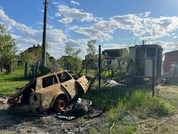 an abandoned truck sits in the grass by a train