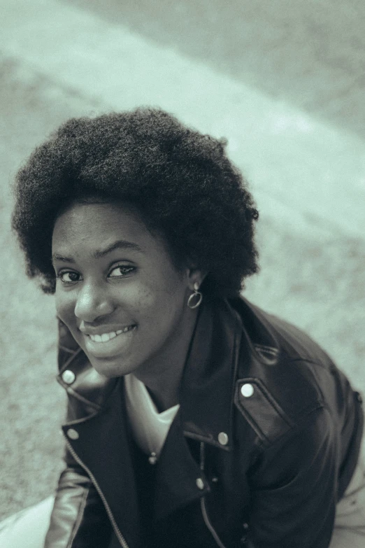 a woman is sitting down wearing a leather jacket and smiling