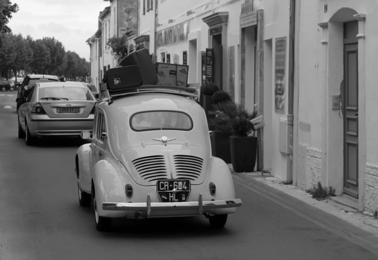 an old car drives down the street with its luggage on top