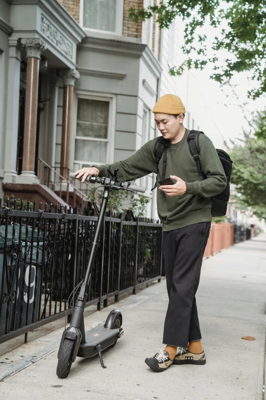 a young man leaning on a street scooter in front of a wrought iron fence